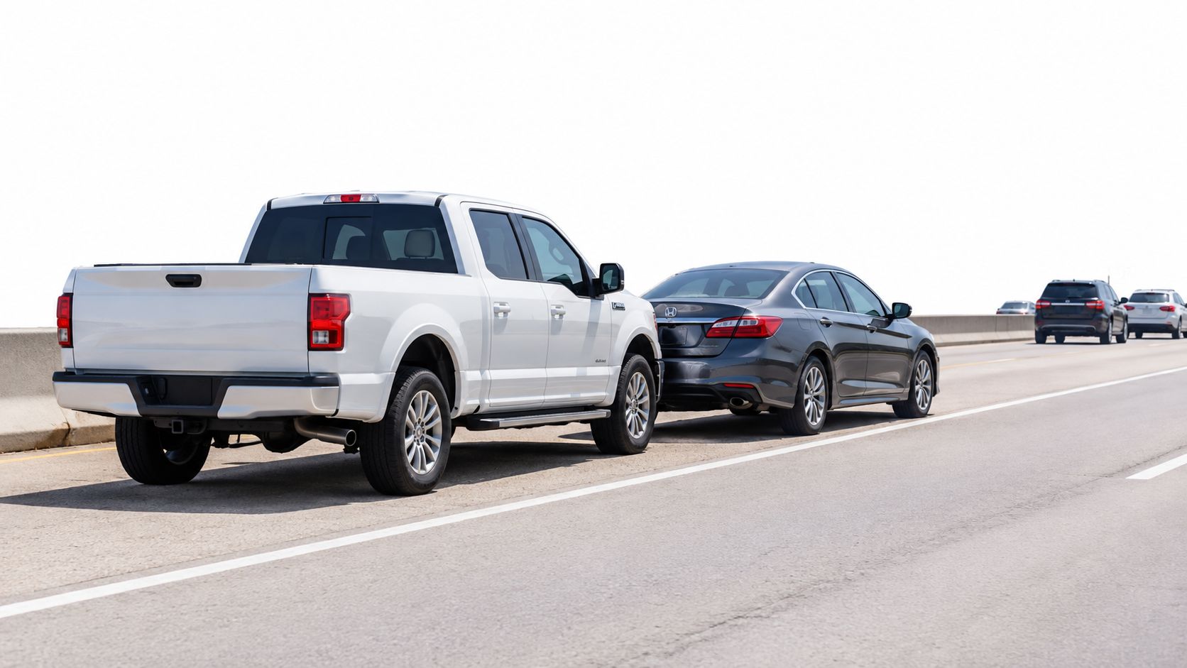 A white pickup truck following closely behind a dark gray sedan on a busy highway.